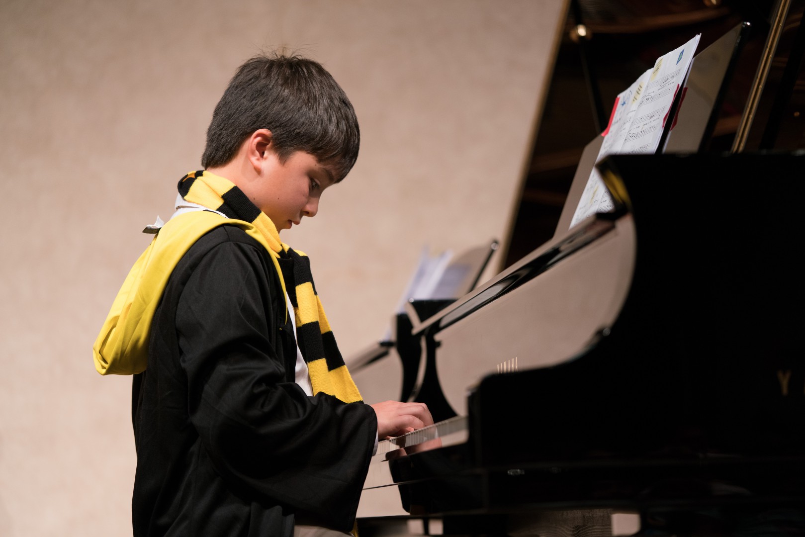 Little boy wearing yellow and black scarf playing the piano